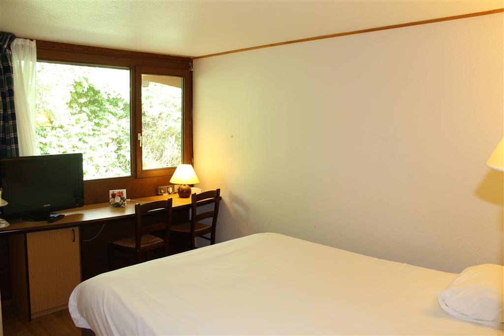 Chambre avec bureau, télévision et fenêtre donnant sur les arbres